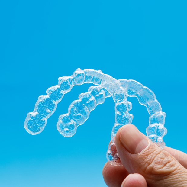Hand holding two clear aligners with a crisp sky blue background