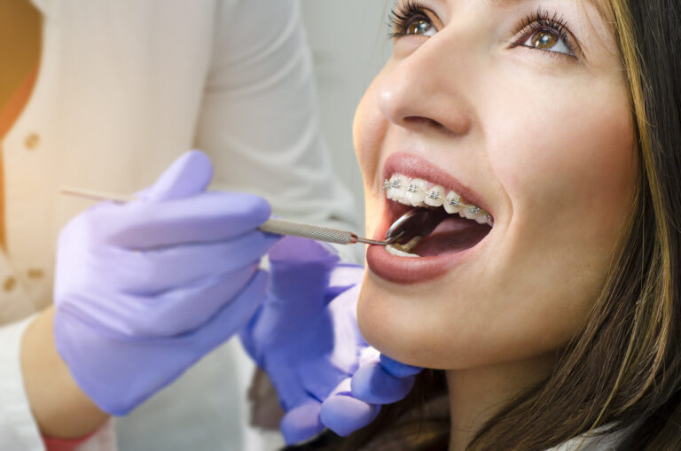Woman having her braces analyzed by her orthodontist with a small dental mirror behind her teeth