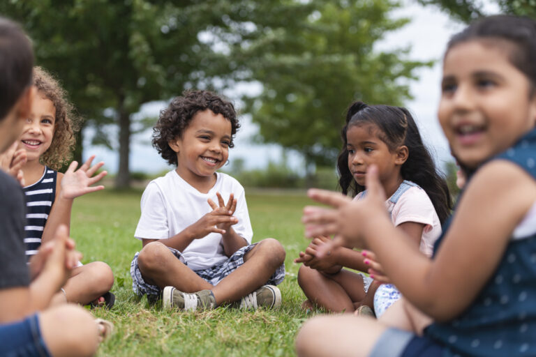 A group of young children sitting in a circle and playing in a field